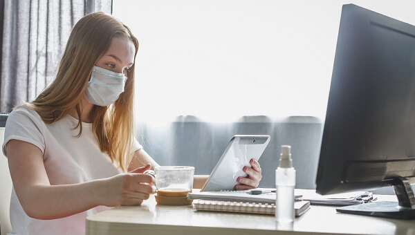 A woman is wearing a mask and reading coronavirus news on her tablet.