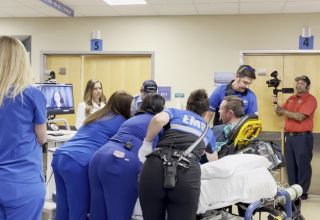 A man is in the hospital, on a stretcher, while a physician and several nurses attend to him.