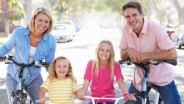 A husband, wife and their two young daughters smile while riding their bicycles