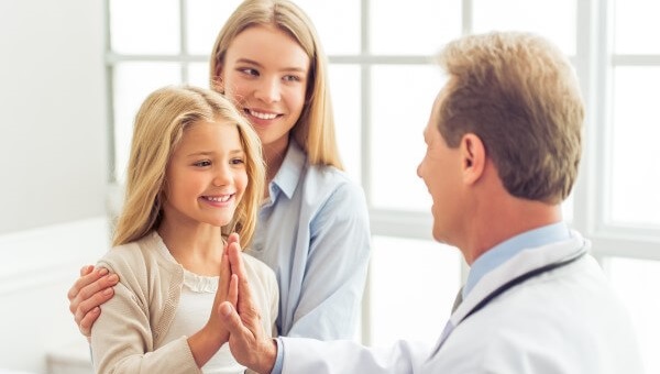 a mother and her daughter smiling and high fiving a doctor