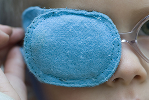 Close-up of young child with blue eye patch over one eye.