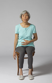 Woman sitting in a chair. She is practicing deep breathing exercises.