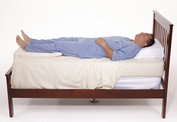 Man lying on back in bed with pillows under legs.