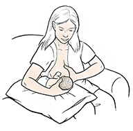 Woman breastfeeding premature baby in football hold.