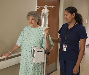 Patient walking in hosptial hallway with healthcare provider.