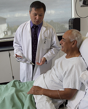 Healthcare provider with electronic tablet talking to man in hospital bed.