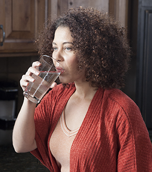 Woman drinking glass of water in kitchen.