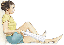 Woman sitting on floor with back against wall. One leg is flat on floor. Woman has towel looped around heel of other foot and is pulling on towel ends to slide heel towards her.