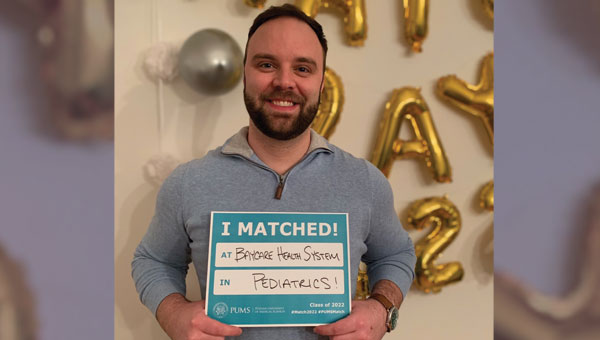 a man holding a light blue sign that reads "i matched!"