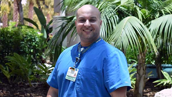 man wearing a baycare blue shirt standing in front of palm trees