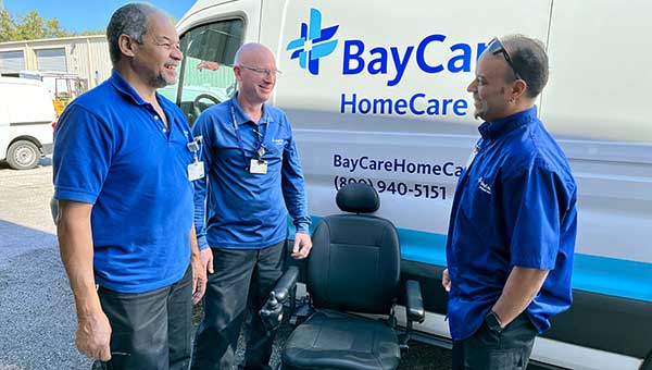 three men wearing blue shirts in front of a baycare van