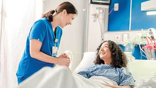 A BayCare Nurse and teenage female patient holding hands and smiling in a hospital room. 