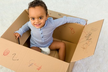 Little toddler boy sitting in a cardboard box playing with crayons