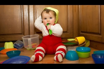 Adorable baby girl pulling pots and pans and other dishes out of a kitchen cupboard