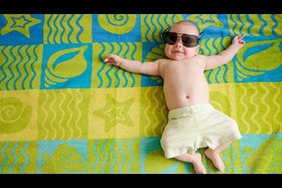 Adorable baby in beach shorts relaxing on a big beach towel smiling
