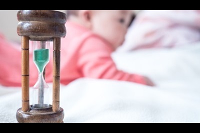 A baby is sitting next to an hourglass