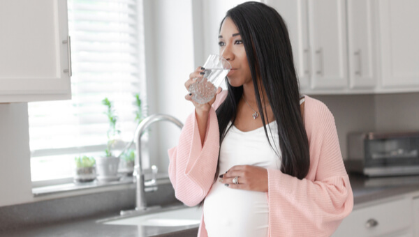 a pregnant woman drinking a glass of water in her kitchen