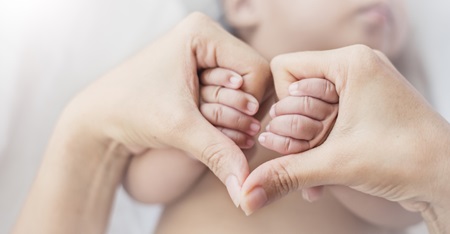 A mom holds her newborn baby's hands.