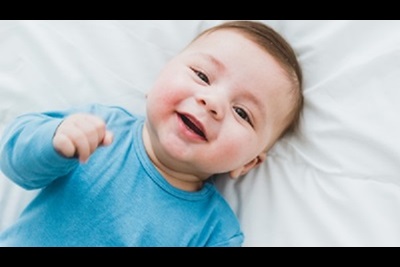 Portrait of an adorable 3 month old baby smiling lying in a bed of white sheets