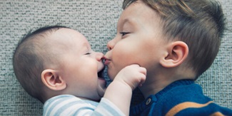 Toddler kissing his happy sibling