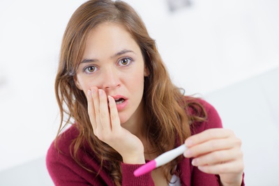 A young woman has a surprised look on her face while holding a home pregnancy test.