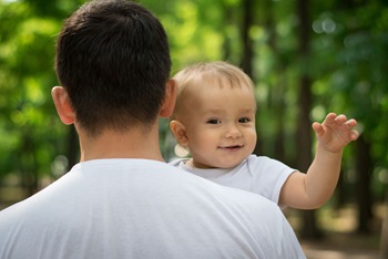 Smiling baby boy waving hand while father holds him in arms