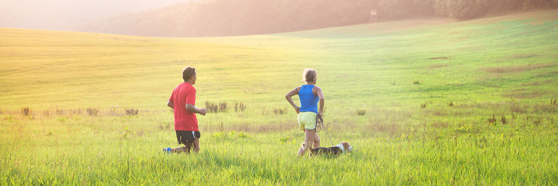 husband and wife jogging through field with their dogs