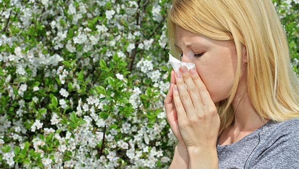 A woman with allergies is blowing her nose into a tissue.