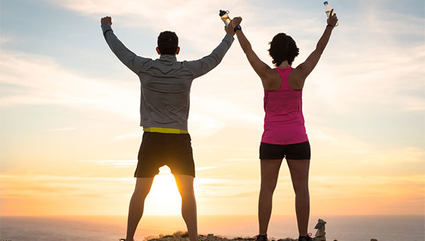 A man and woman celebrate their weight loss goals while watching the sunset.