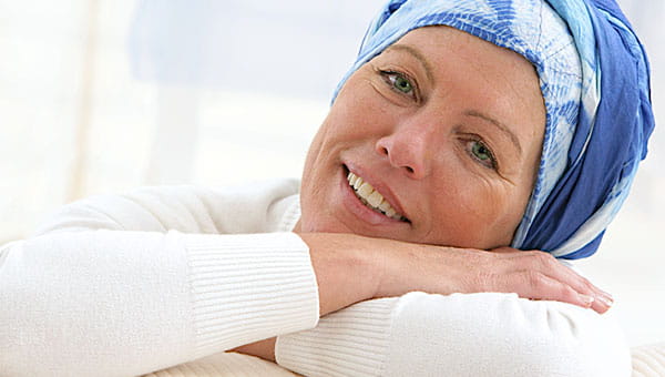 A smiling lady resting her head on her shoulder with arms crossed with a head scarf on.