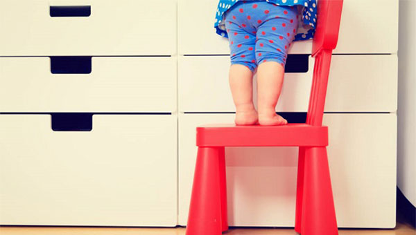 A toddler is standing on a step stool to reach something on a counter.