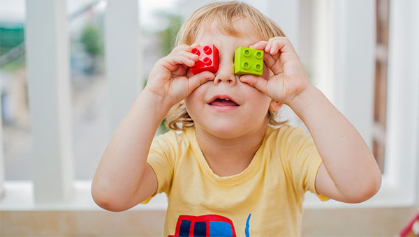 A young boy hold two Lego blocks over his eyes.