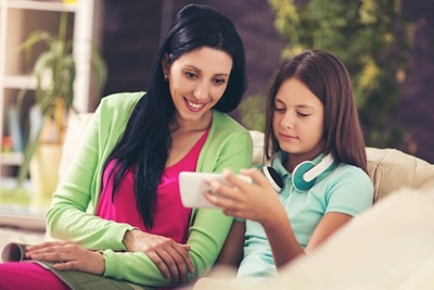 Mother and daughter sitting on the couch, looking at a mobile device