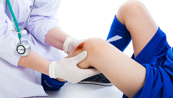 A doctor treats a wound on the knee of a young athlete.