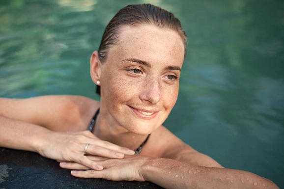 A woman with sun spots is swimming at a pool.