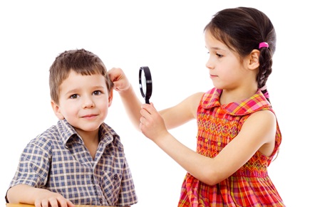 A little girl examines a little boy's ear with a magnifying glass