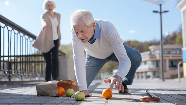 A senior man tripped while walking on the sidewalk and dropped his bag of groceries.