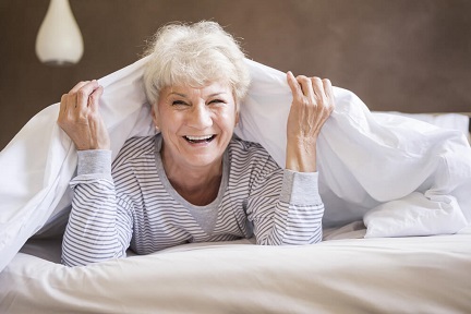 A senior woman is smiling while resting on her bed.