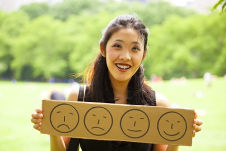 A woman is holding up a sign that has happy and sad faces on it.