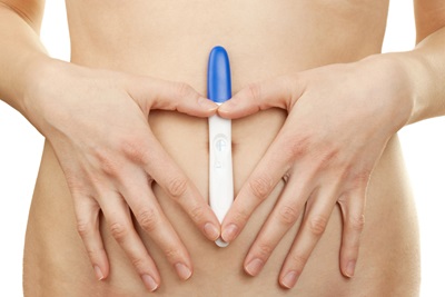 A woman is holding a home pregnancy test to her abdomen.