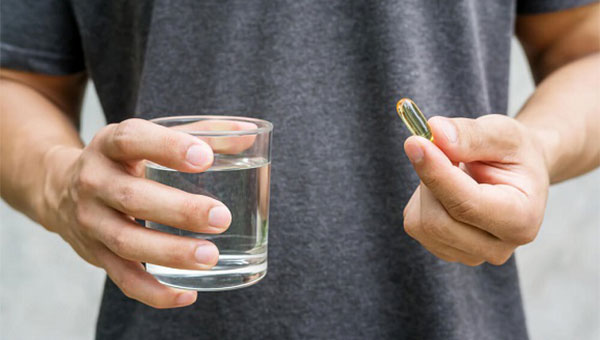 A man is holding a fish oil supplement pill and a glass of water.