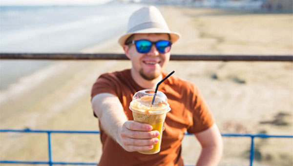 A man is drinking a caffeinated beverage at the beach.
