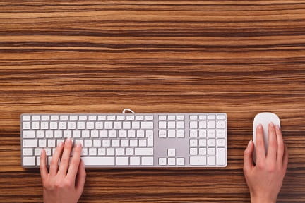 Hands using a white keyboard and mouse at a desk