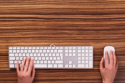 Hands using a white keyboard and mouse at a desk