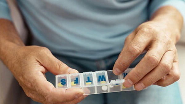 A person acquiring their medication from a daily pillbox