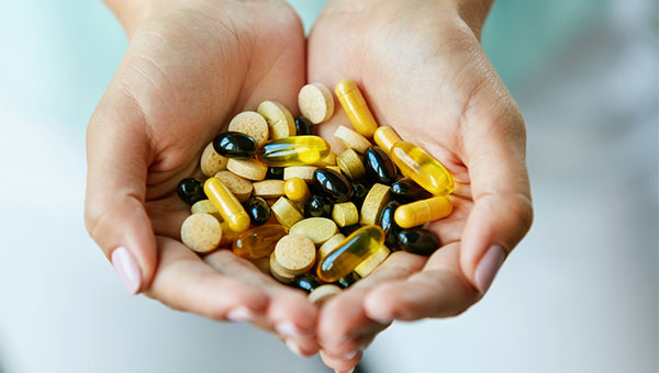 A woman is holding various vitamin pills in her hands.