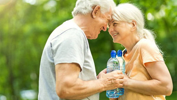 two exercising seniors with water bottles smiling while touching foreheads