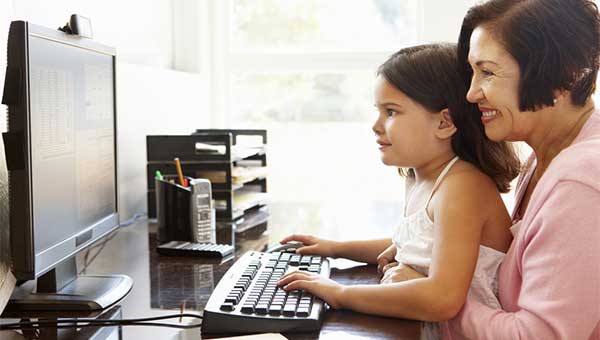 A grandmother helps her young granddaughter as she types on a computer keyboard.