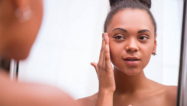 A young woman is looking in the mirror and putting lotion on her face.