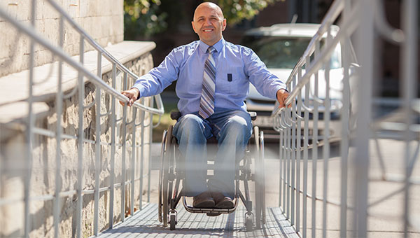 A man in a wheelchair is going up a ramp to enter a building.